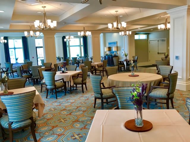 A spacious and elegantly decorated dining room with multiple tables and chairs, featuring floral centerpieces and warm lighting.
