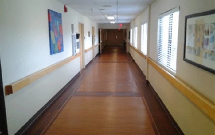 An empty corridor in a hospital with wooden flooring and window blinds.