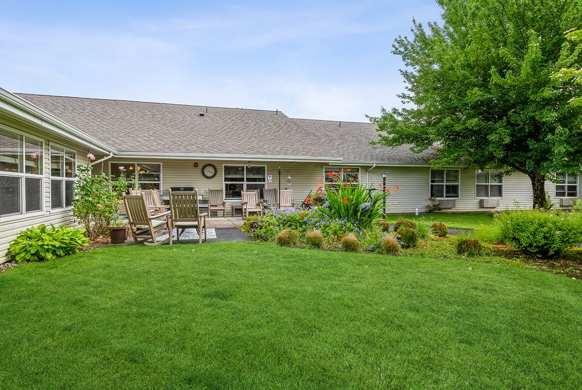 A well-maintained backyard with a lush lawn, patio area, and garden plants in front of a single-story house.