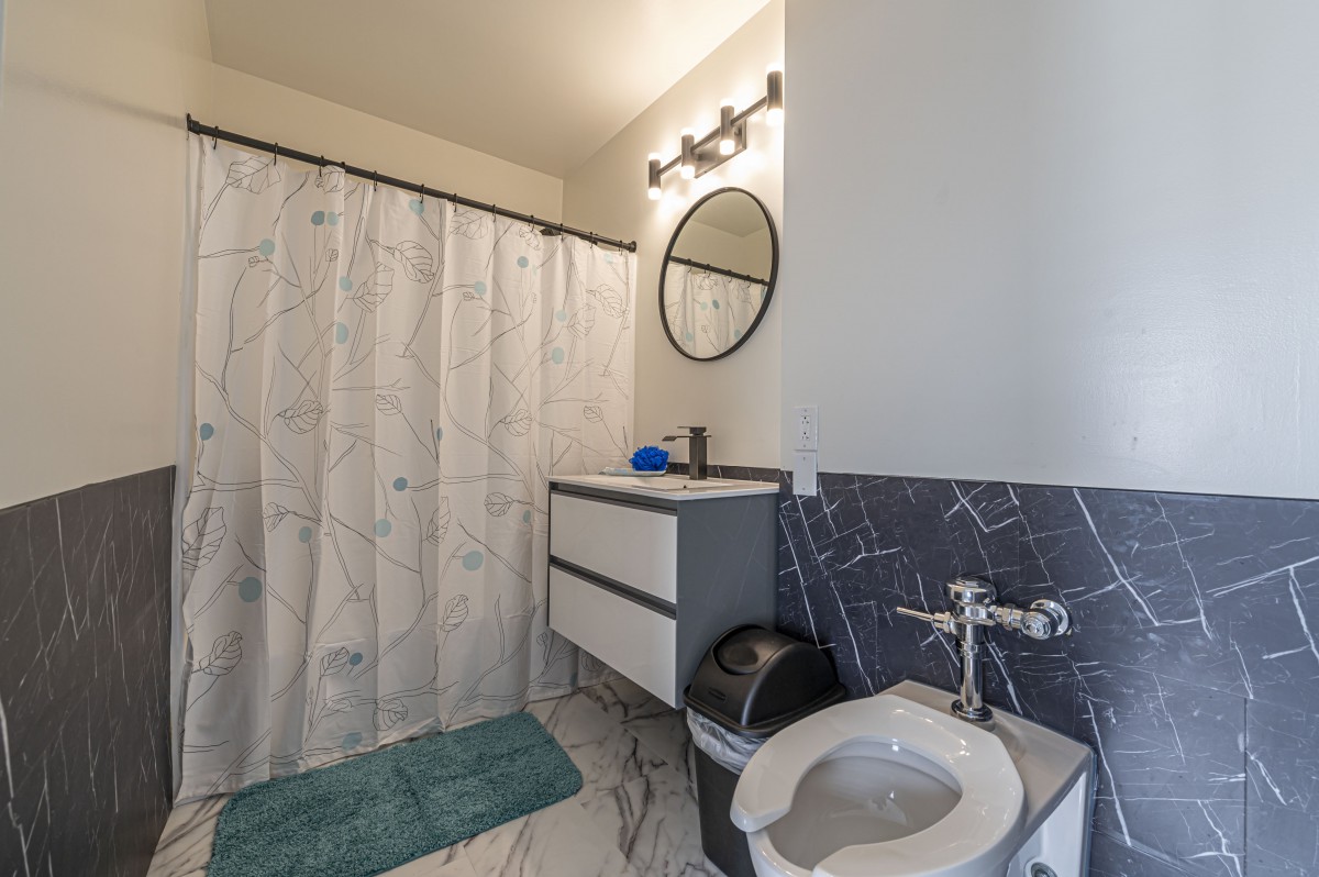 A modern bathroom with a white shower curtain, round mirror, and vanity.