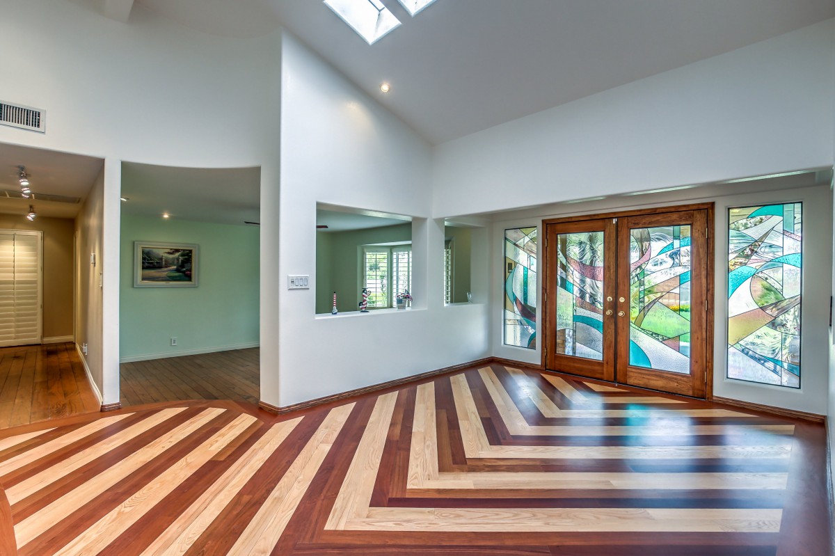 A modern living room featuring a striking wooden floor pattern, large glass doors, and abundant natural light from a skylight.