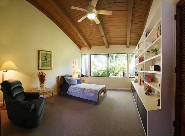 A cozy bedroom with a wooden ceiling and large windows overlooking greenery.