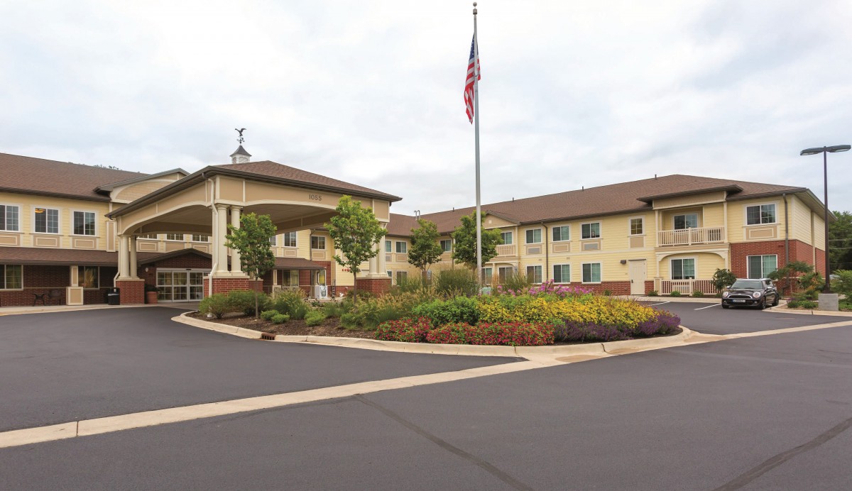 A view of a large building with an American flag, surrounded by landscaped gardens and parking area.