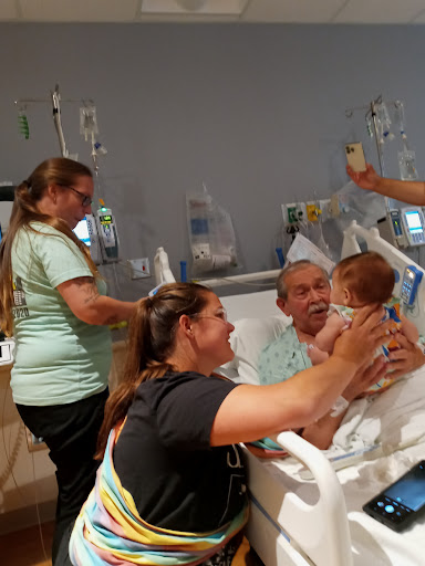 A heartwarming family visit in a hospital room, where a baby is brought to share precious moments with a patient.