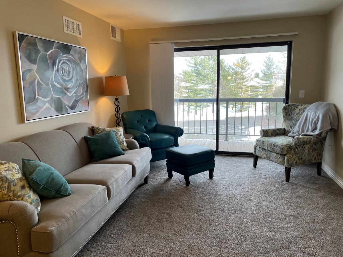 A cozy living room with a sofa, armchairs, and a large sliding door letting in natural light.