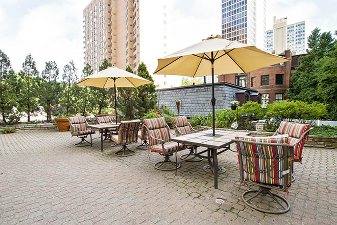 A charming outdoor patio with tables, chairs, and umbrellas set against a city backdrop.