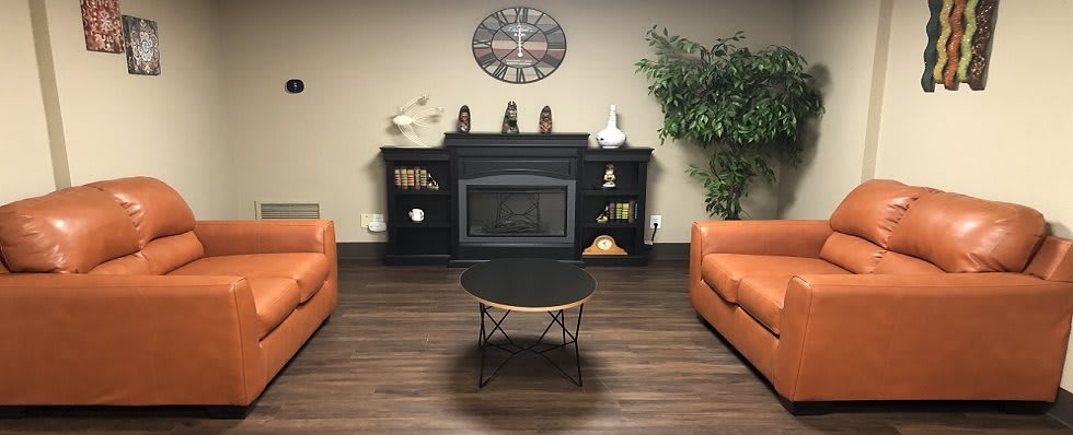 A cozy living room setup featuring a fireplace, two orange armchairs, a central coffee table, and decorative elements on the shelves.
