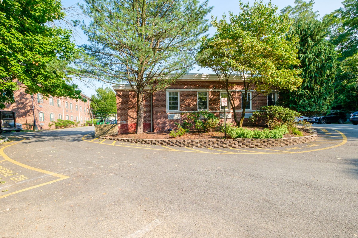 A small brick house surrounded by trees and landscaping, located in a suburban setting with a driveway.