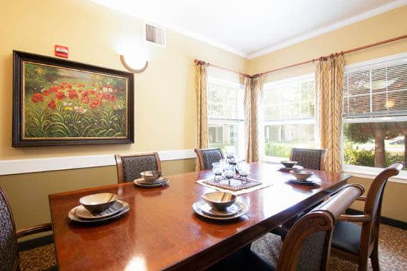 A well-lit dining room with a large wooden table set for a meal, surrounded by chairs and adorned with a painting on the wall.