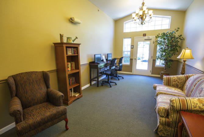 A cozy office space featuring computers, comfortable seating, a bookshelf, and a chandelier near the entrance.