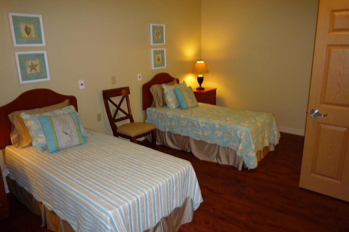 A cozy bedroom with twin beds, a lamp, and wooden flooring.