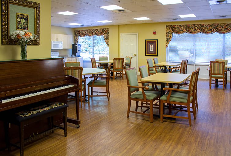 A cozy dining area with a piano, tables, and chairs on a wooden floor.