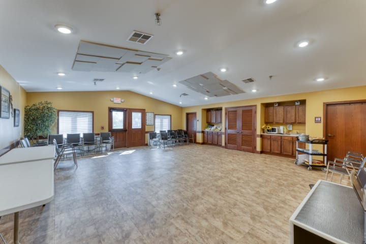 A spacious community center meeting room with chairs, wooden cabinets, and bright lighting.