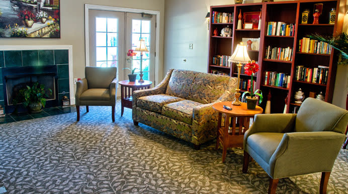 A cozy living room with a sofa, chairs, and a bookshelf, illuminated by lamps.