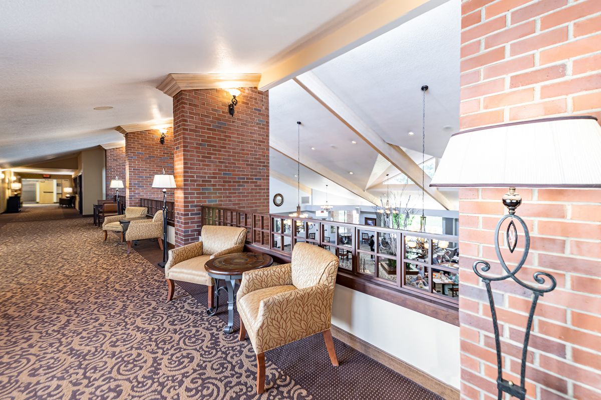 A cozy lounge area with comfortable chairs and a brick wall, featuring warm lighting and carpeting.