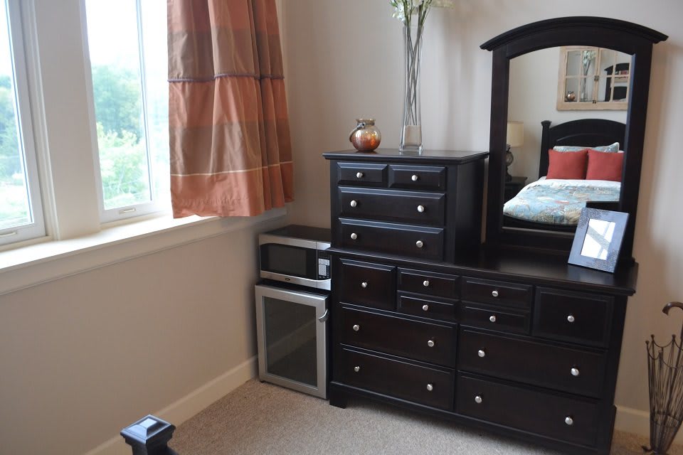 A cozy bedroom corner featuring a dresser with a mirror, adjacent to a window with draped curtains.
