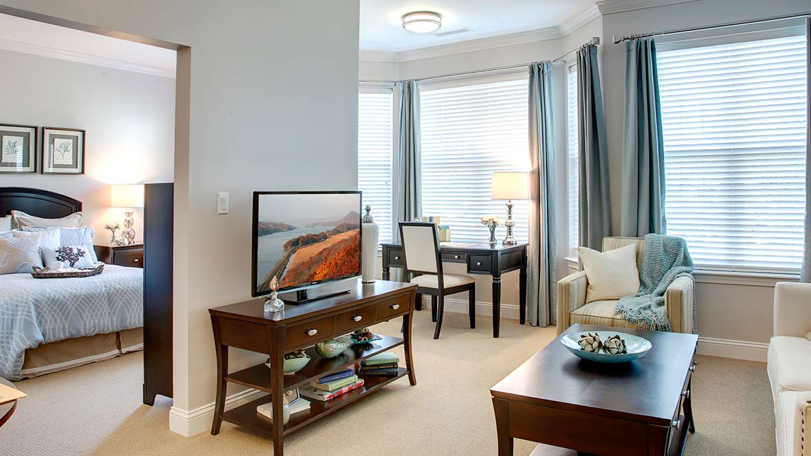 A cozy living room with elegant furniture, featuring a television and large windows with curtains.