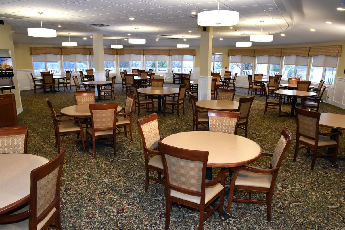 A spacious dining area with multiple round tables and chairs arranged neatly under ceiling lights.