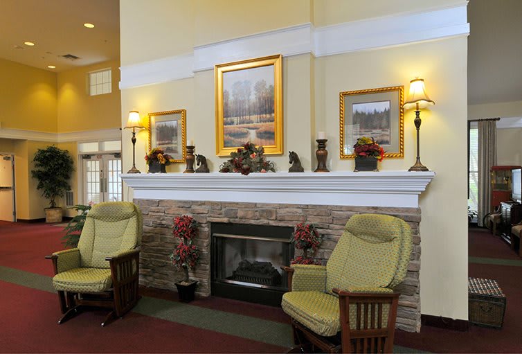 A cozy living room with a fireplace, armchairs, and decorative paintings.
