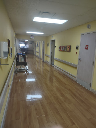 A view of a hospital hallway with yellow walls and polished floors, featuring a patient cart.