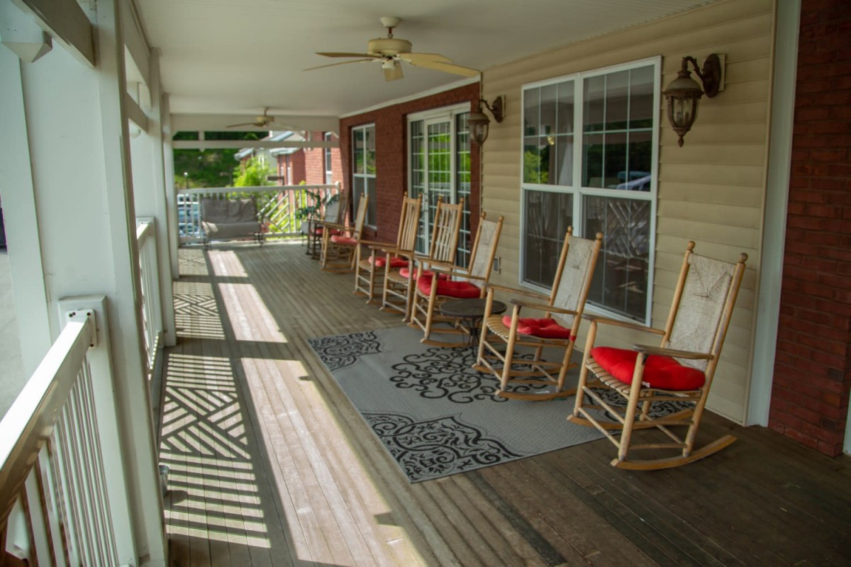 A cozy covered porch with several rocking chairs and a wooden deck.