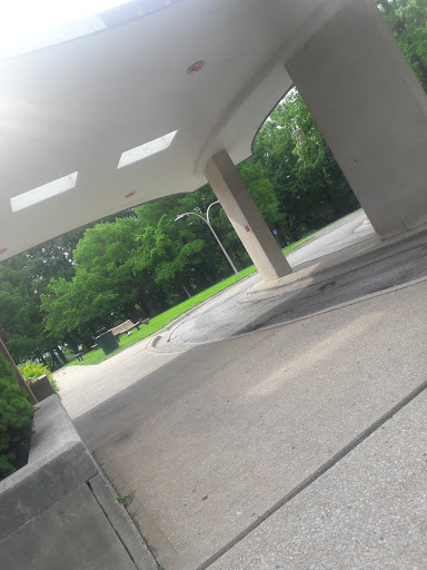 A serene walkway under a modern architectural structure, surrounded by lush greenery.