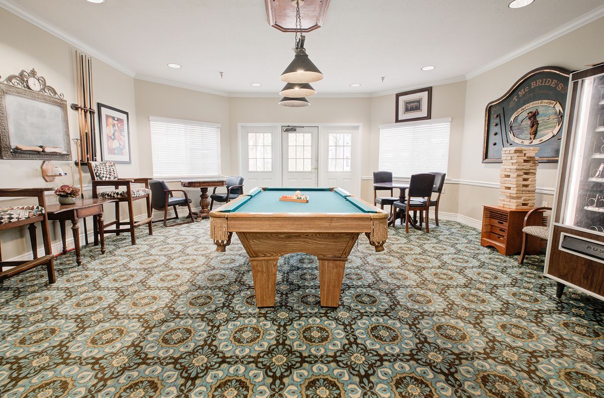 A well-lit game room featuring a central pool table surrounded by seating and stylish decor.