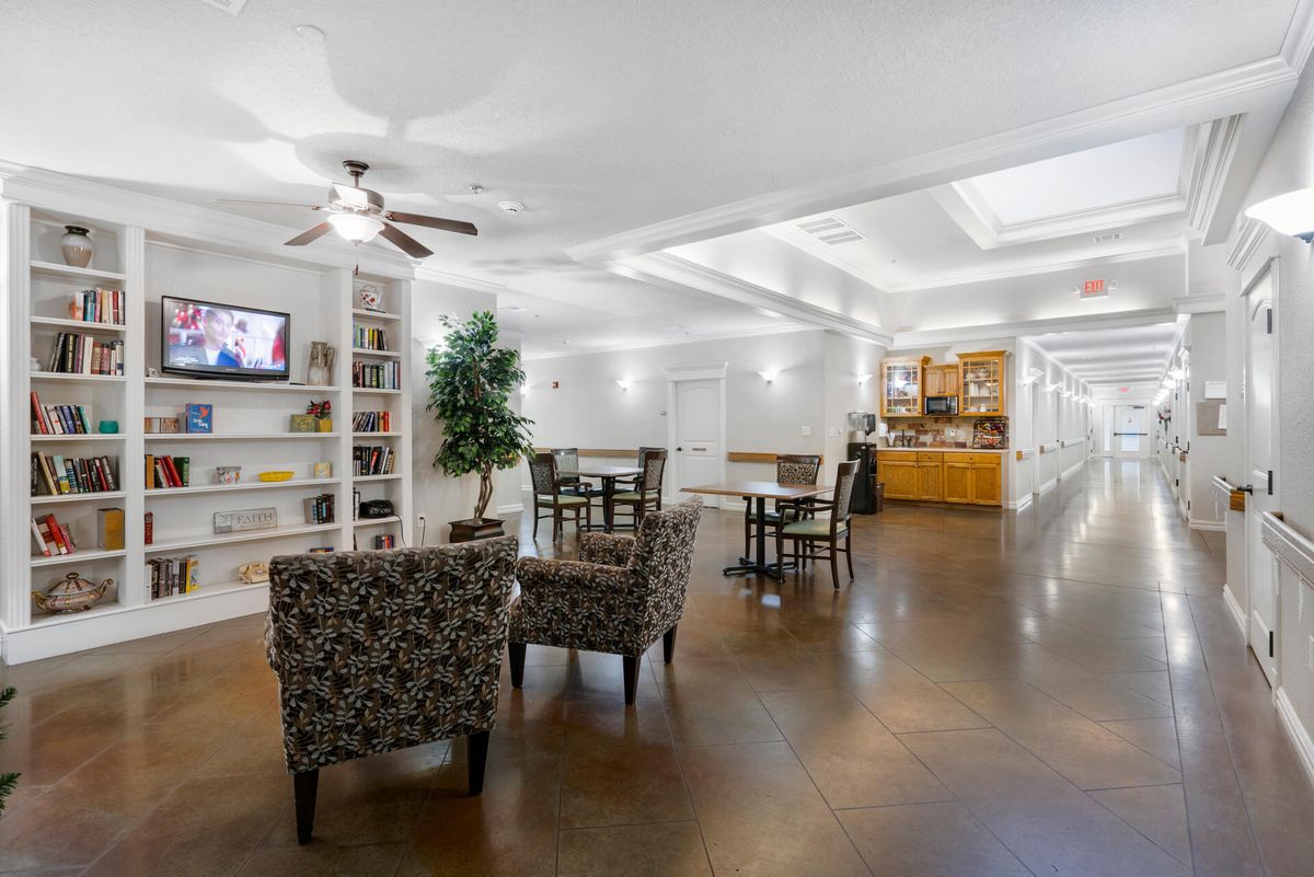 A cozy and well-lit living space featuring comfortable seating, a television, bookshelves, and a kitchenette.