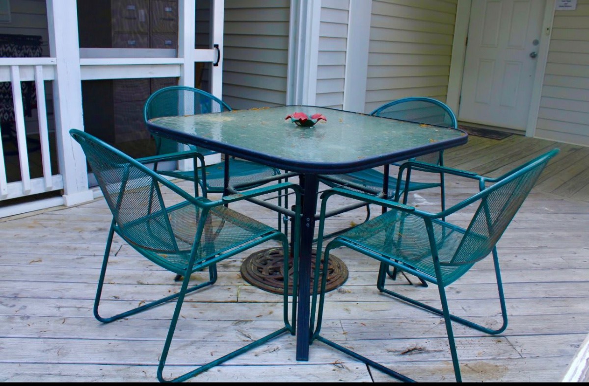 A set of outdoor patio furniture with a glass table and four metal chairs on a wooden deck.