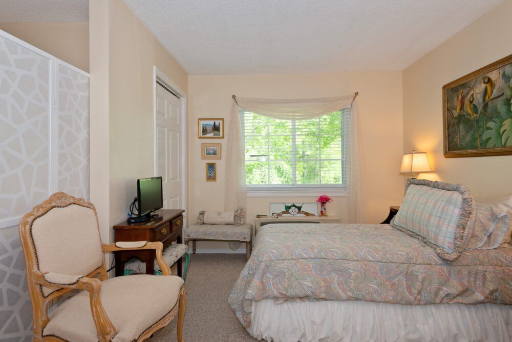 A cozy bedroom with a neatly made bed, a small television, and a bright window that lets in natural light.