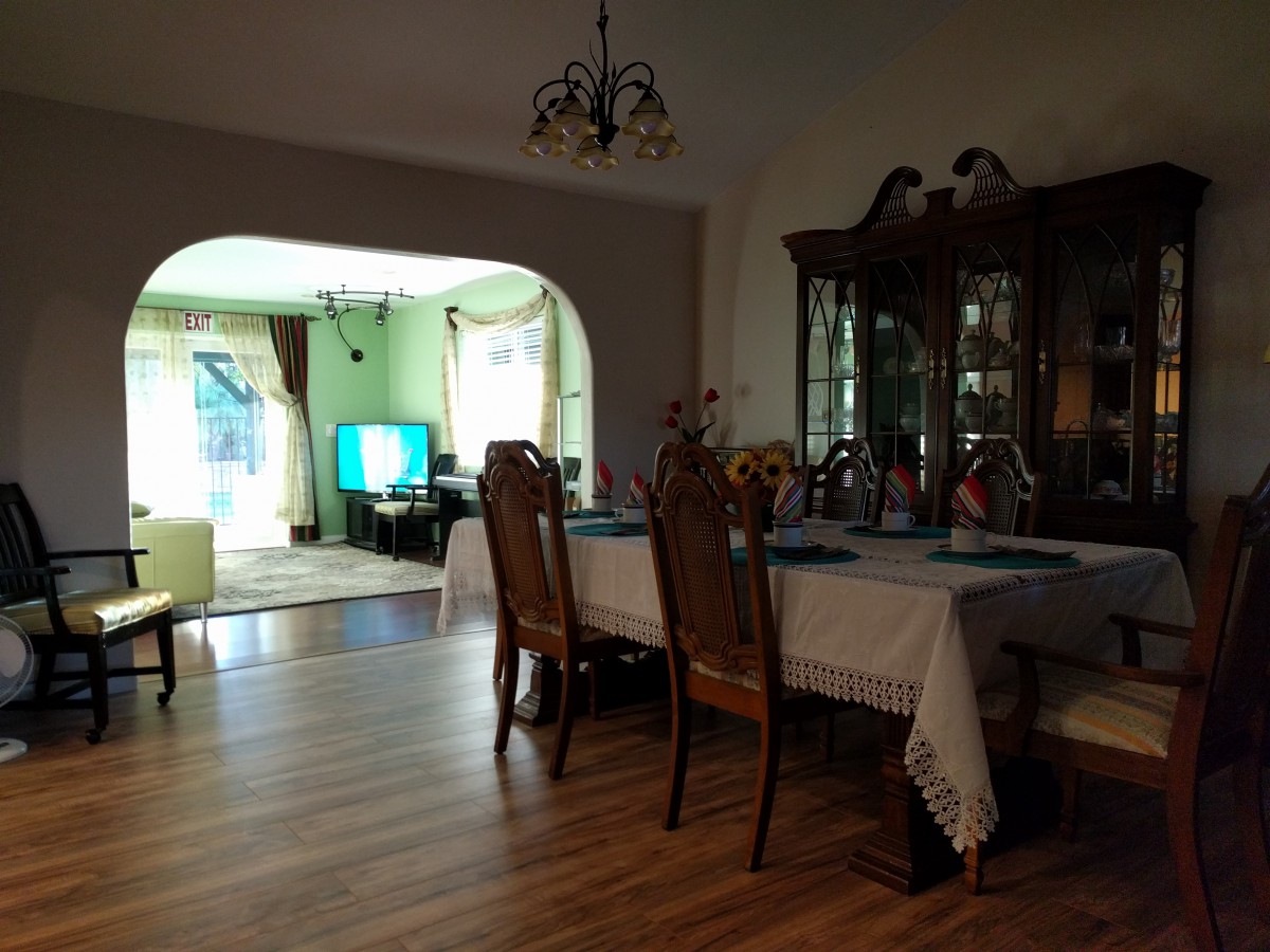 A cozy dining area with a wooden table and chairs, adjacent to a living room featuring a television.