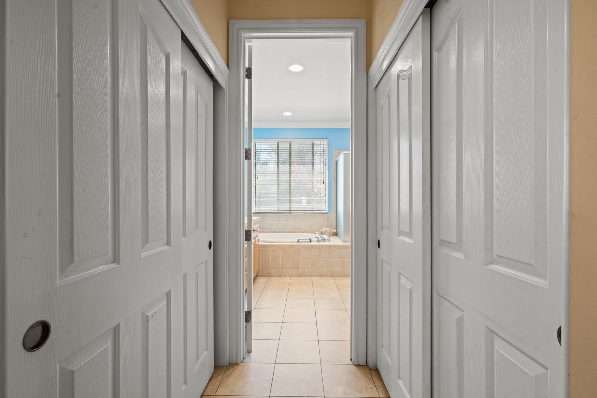A hallway with multiple doors leading to a bathroom at the end.