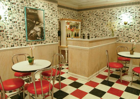 A retro-themed diner with red and white seating, a checkerboard floor, and vintage decor.