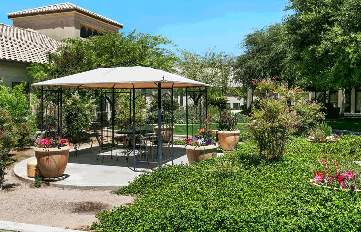 A tranquil garden setting with a gazebo and outdoor furniture, surrounded by lush greenery.