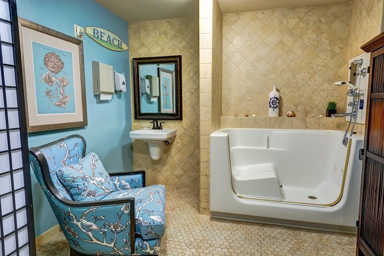 A cozy bathroom with a walk-in tub, sink, and comfortable chair for relaxation.