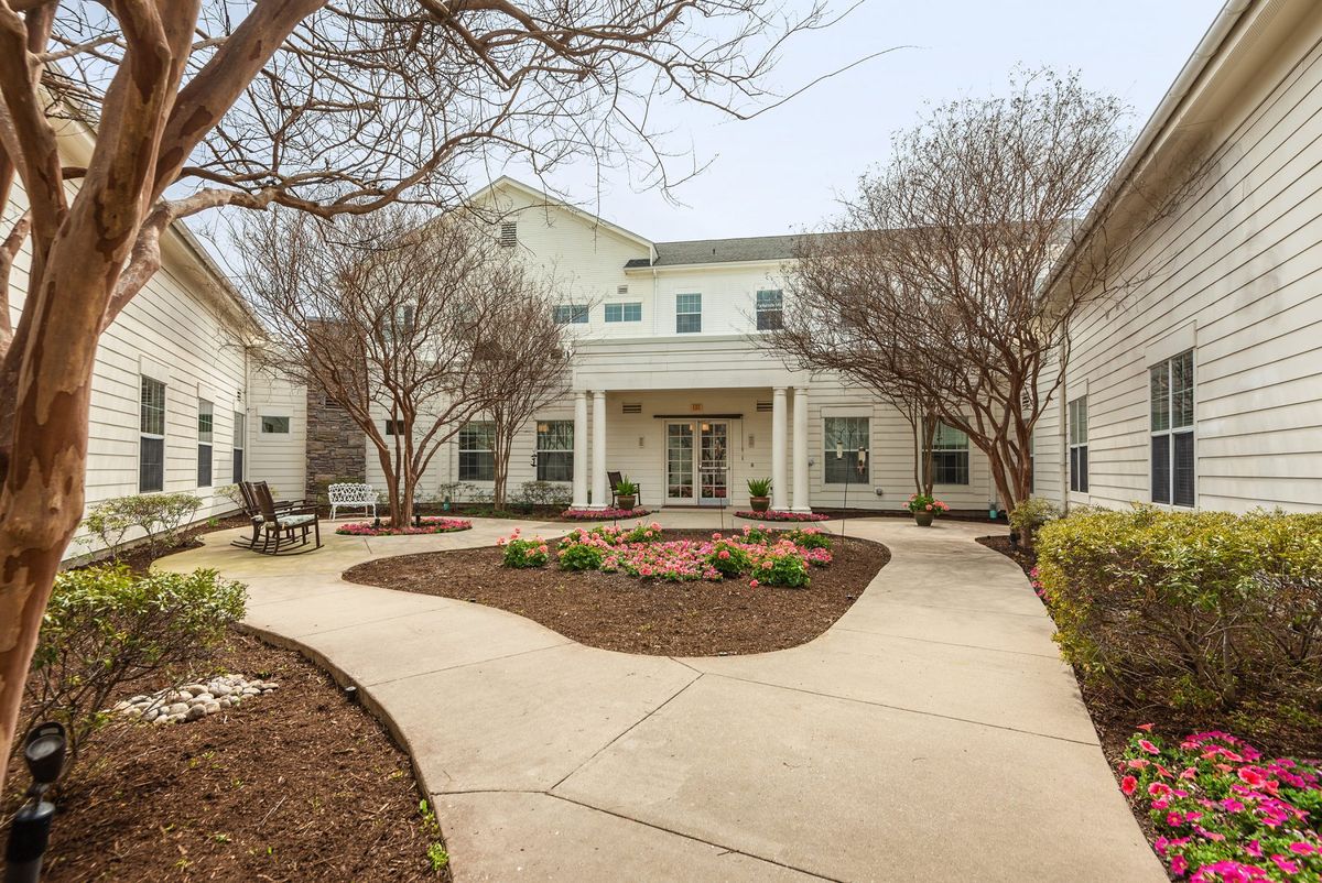 A welcoming entrance to a residential building with manicured landscaping and a curved pathway.