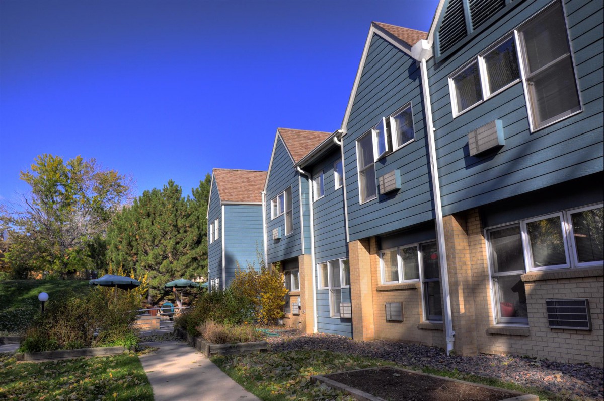 A row of modern townhouses with blue siding under a clear, blue sky.