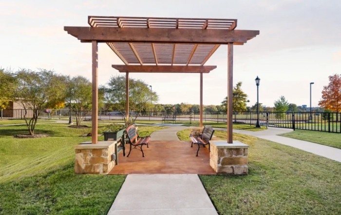 A park pergola with benches and a pathway surrounded by grass.