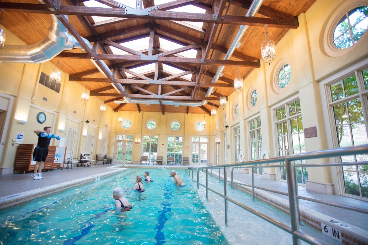 People enjoying swimming in an indoor pool with a vaulted wooden ceiling and large windows.