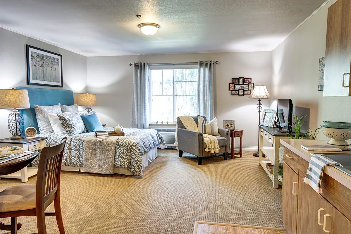 A cozy bedroom with a neatly made bed, comfortable seating, and warm lighting.