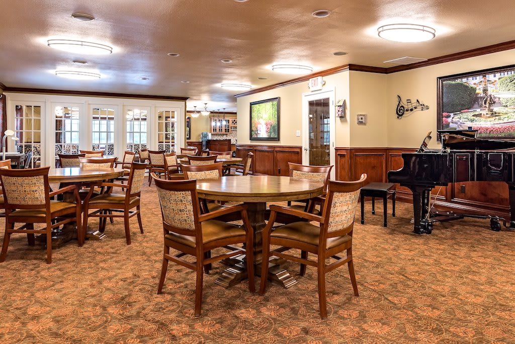 A spacious dining room with wooden tables and chairs, featuring a piano in the corner.