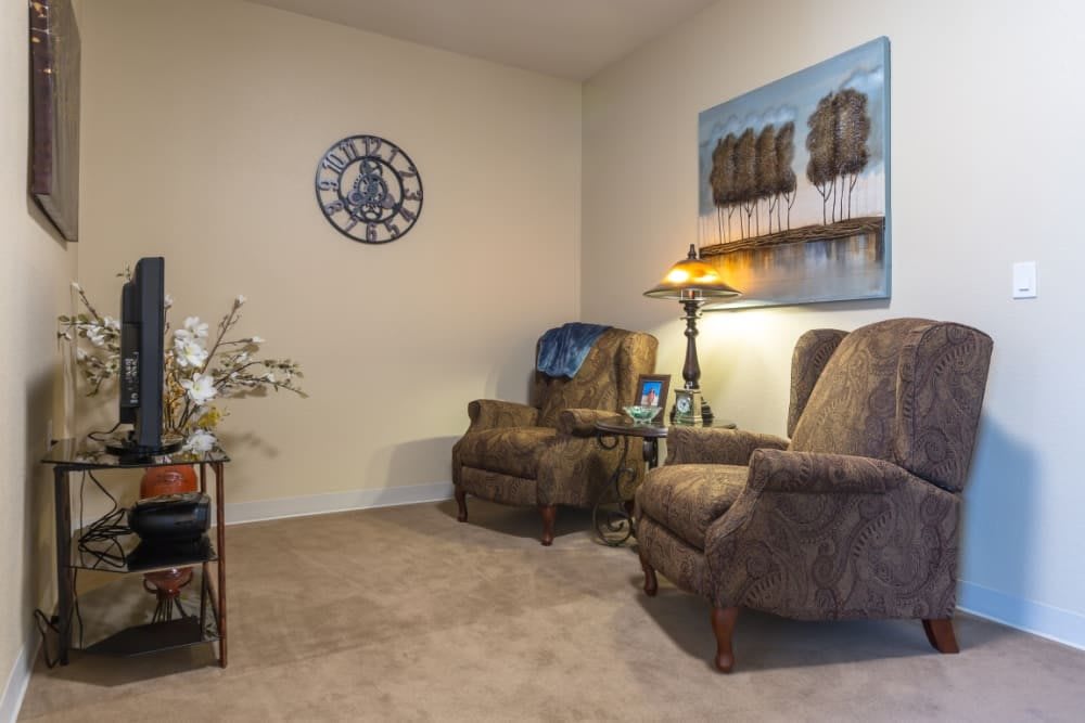 A cozy living room with two armchairs, a floor lamp, decorative wall art, and a clock.