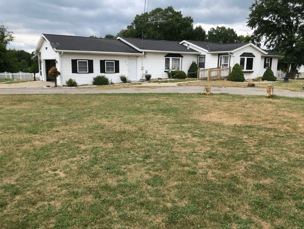 A suburban house with a large front lawn under cloudy skies.