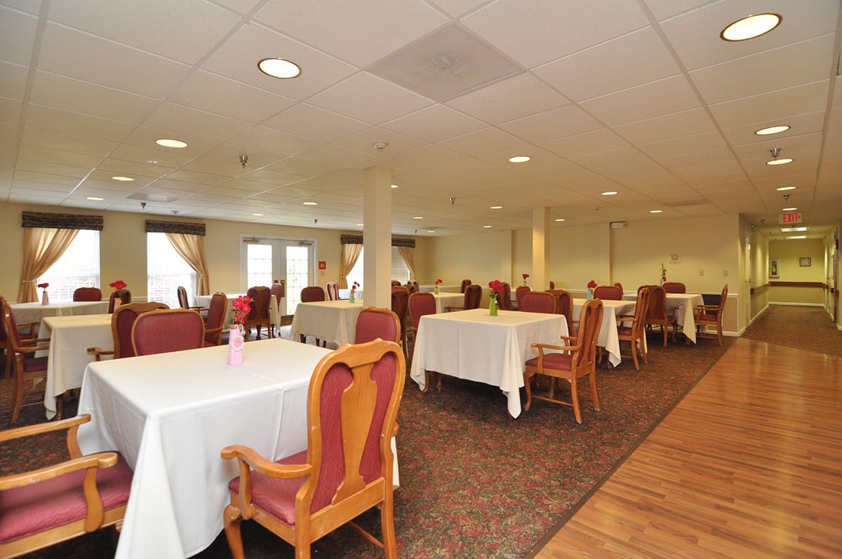 A spacious dining room with tables covered in white tablecloths and surrounded by chairs.