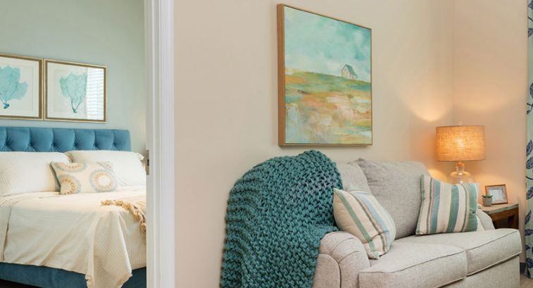 A cozy living room corner featuring a sofa with pillows and a textured blanket, complemented by a landscape painting on the wall.