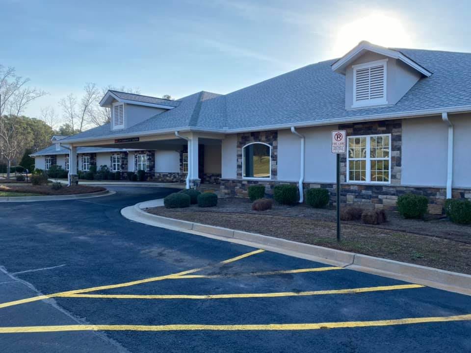 A view of a modern building with a driveway and parking lot on a sunny day.