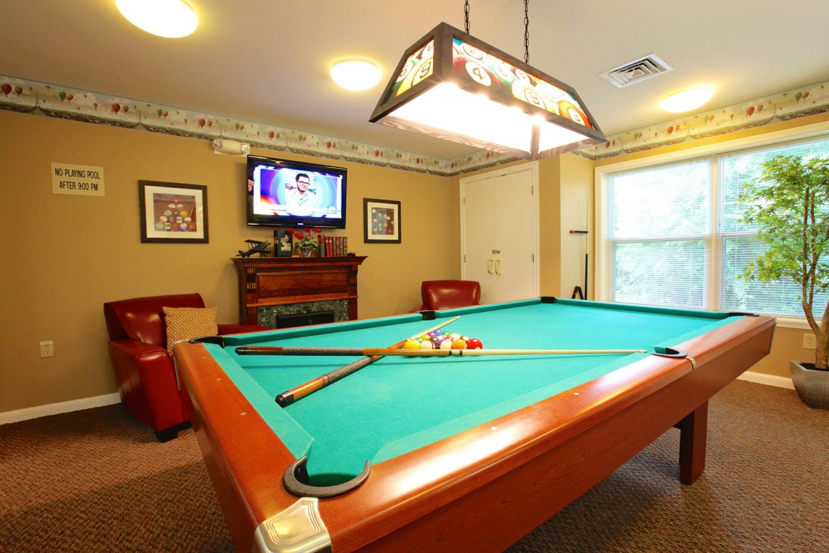 A cozy game room featuring a pool table, wall-mounted TV, and comfortable seating.
