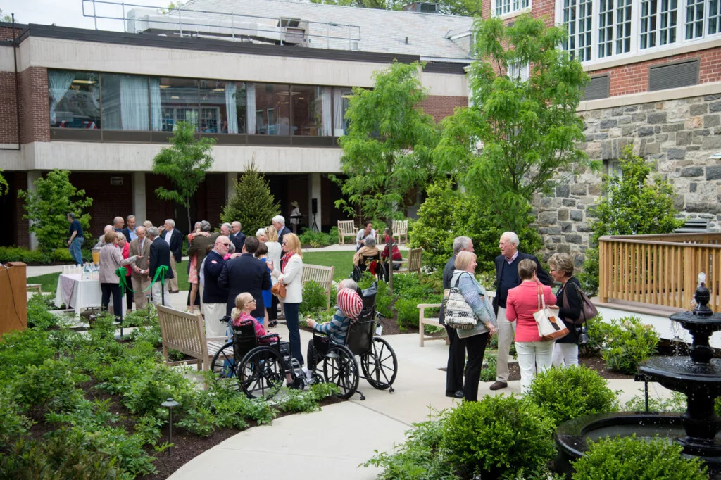 A group of people enjoying a social gathering in a garden setting, with some individuals using wheelchairs.