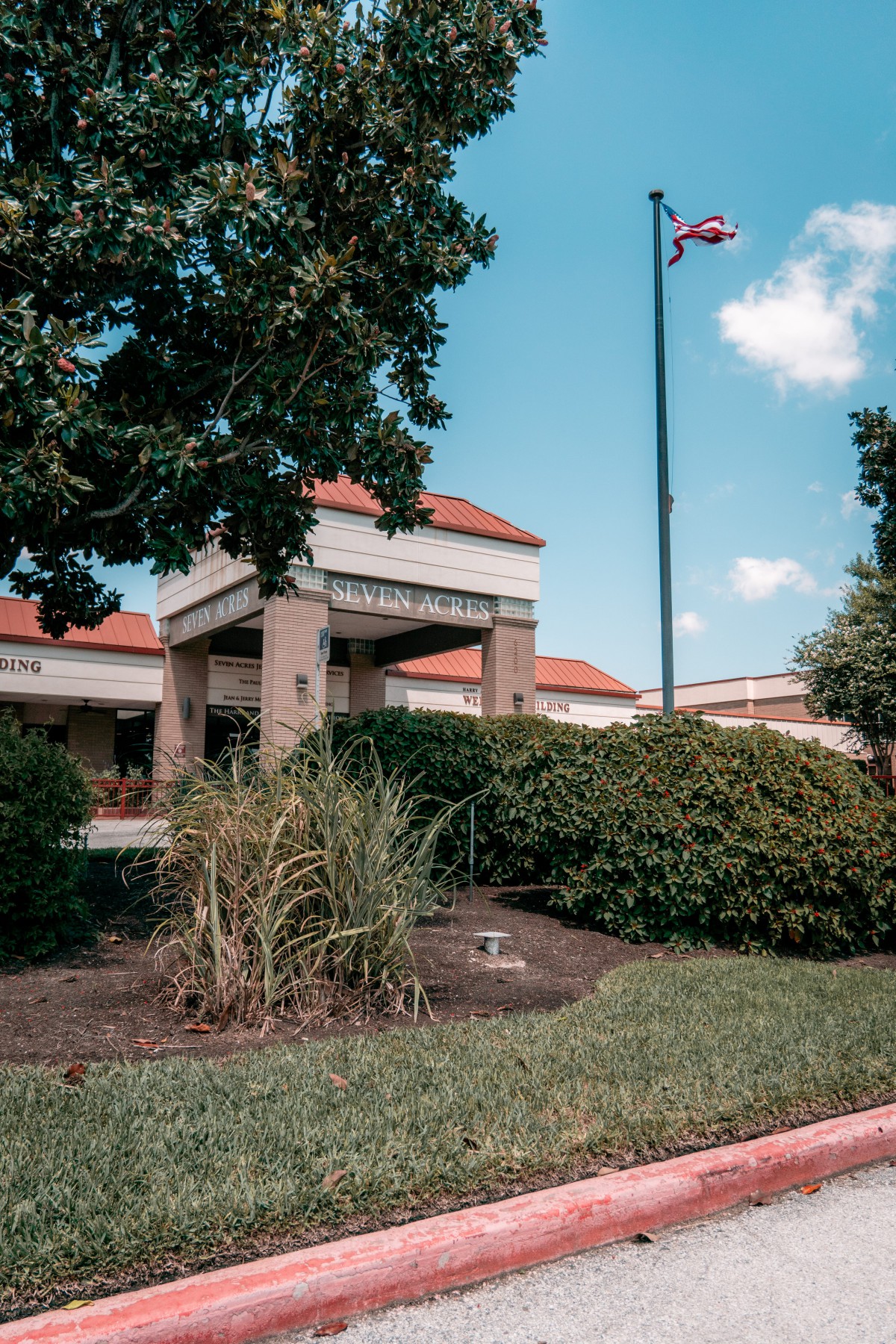 The entrance of a library surrounded by well-maintained landscaping and a flagpole.