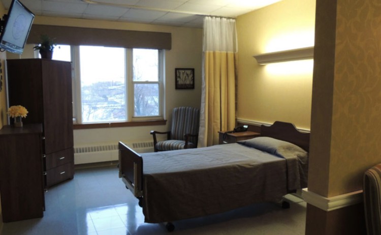 A minimalist hospital room with a single bed, chair, and window.